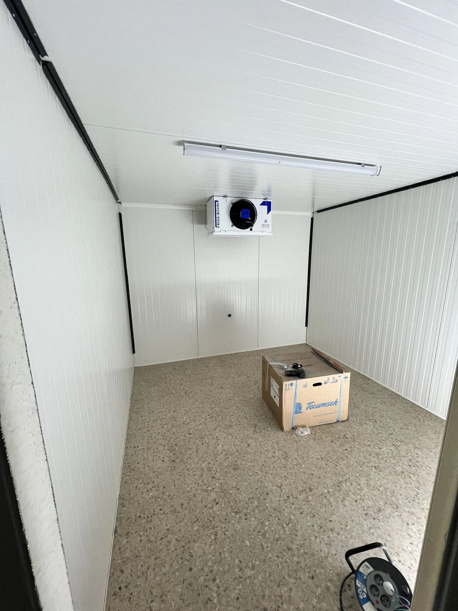 Chambre froide compacte en panneaux blancs, évaporateur mural et carton de matériel au sol