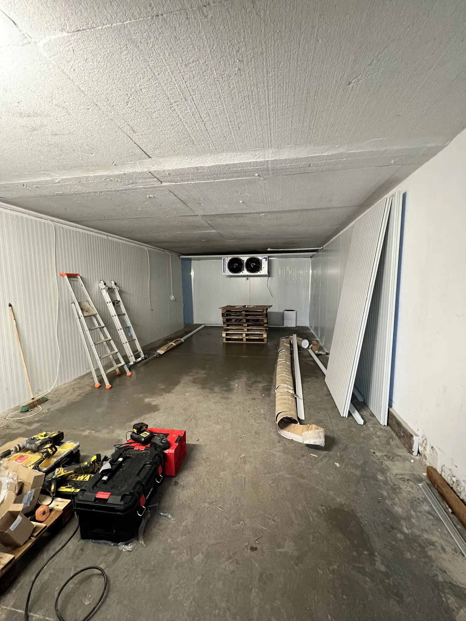 Montage de la chambre froide : panneaux sandwich blancs en cours de pose, échelle, outillage et évaporateur double ventilateur au fond