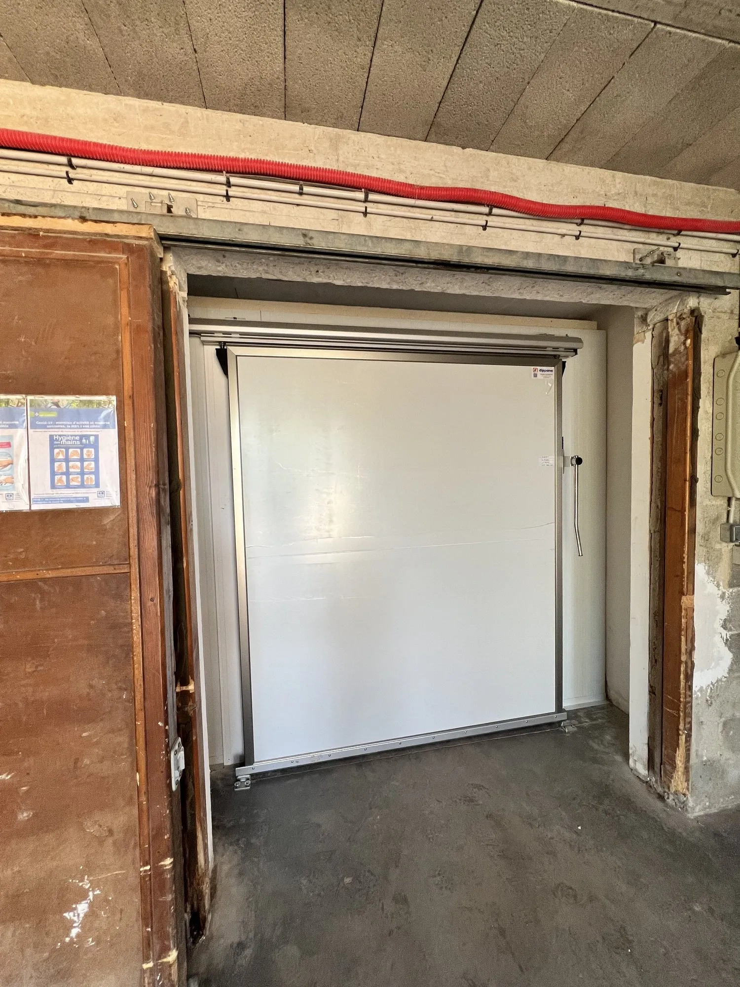 Ouverture de garage en sous-sol donnant sur la chambre froide en panneaux blancs et ses tuyauteries