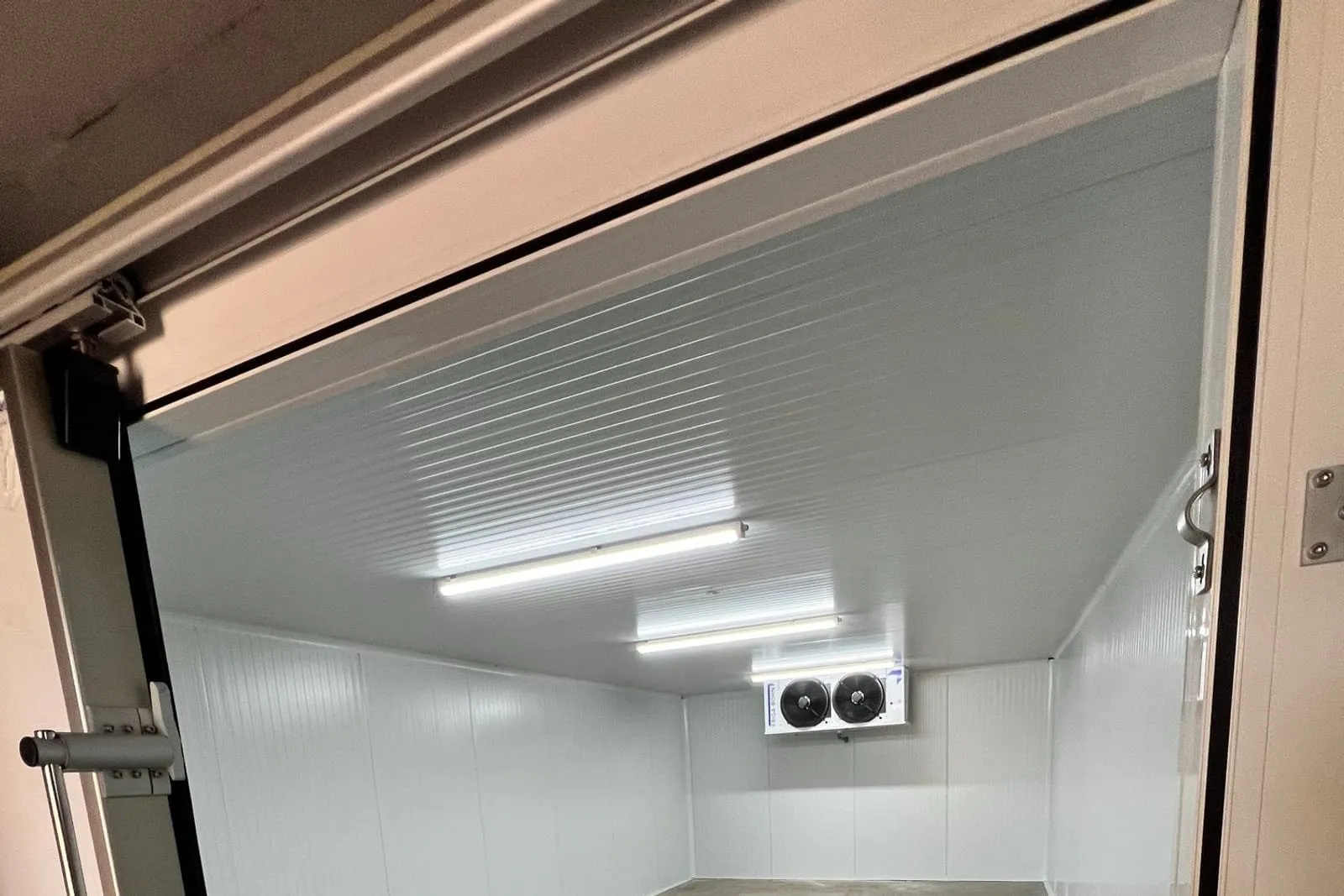 Chambre froide neuve en panneaux sandwich blancs, porte pivotante isotherme ouverte et évaporateur double ventilateur