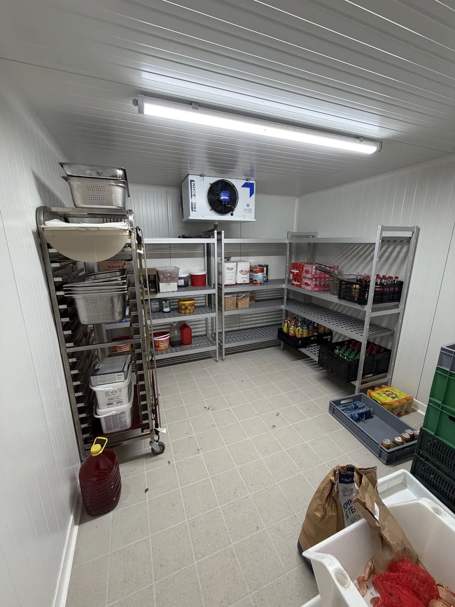 Chambre froide positive de restaurant : rayonnages inox garnis de denrées et de boissons, évaporateur plafonnier, sol carrelé beige