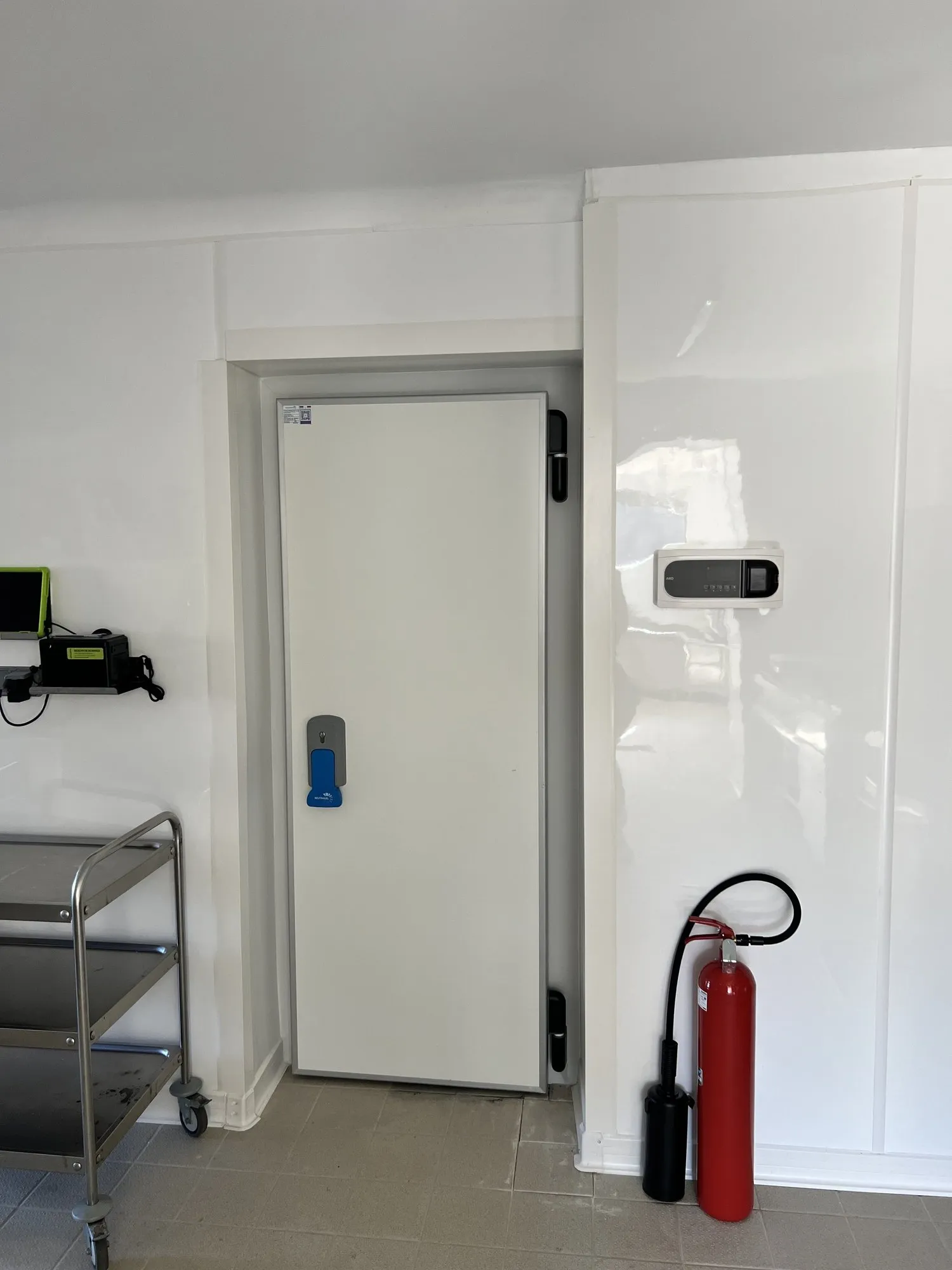 Porte isotherme blanche fermée dans le couloir carrelé, extincteur rouge à côté