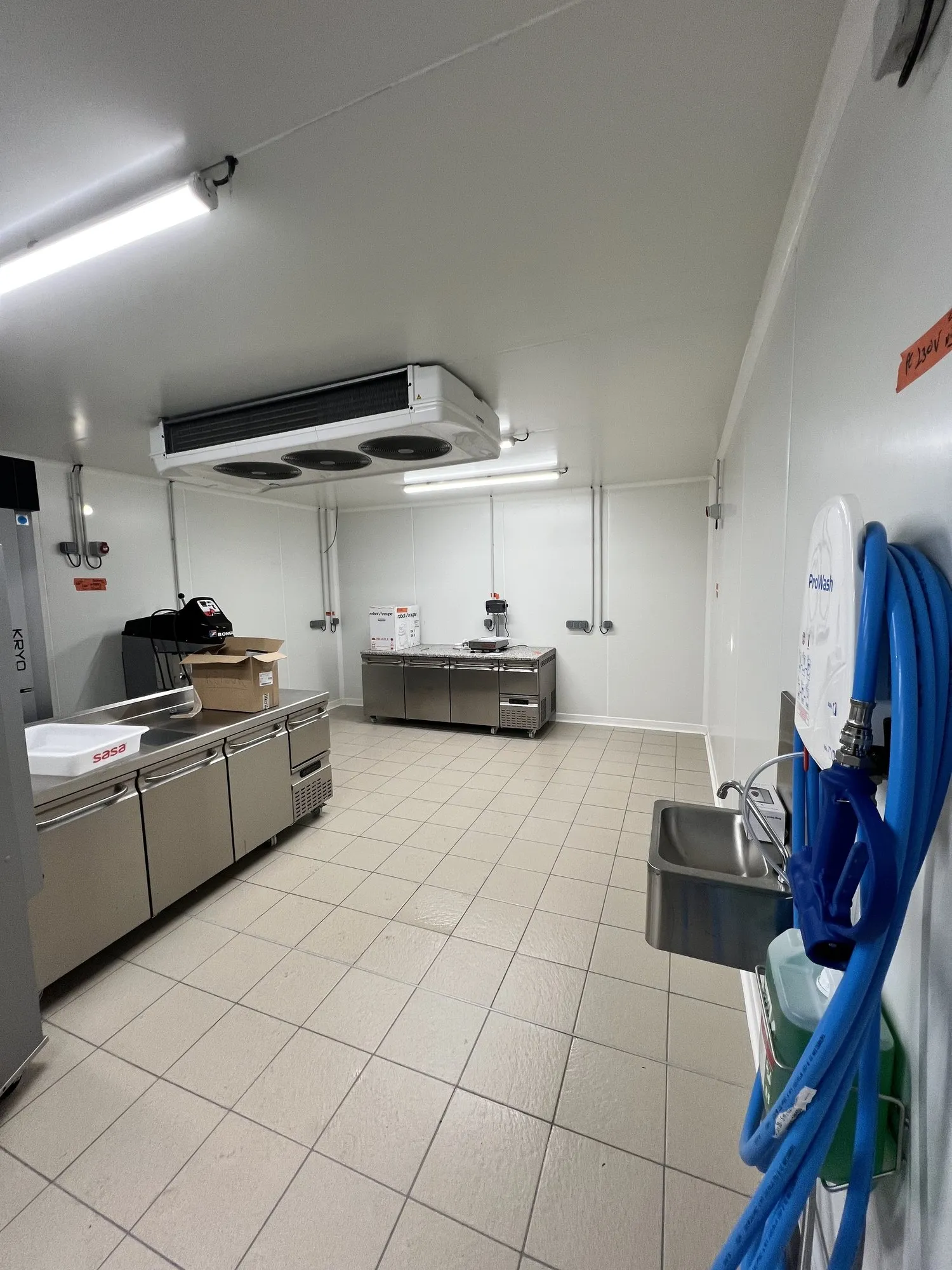 Vue d'ensemble de la cuisine professionnelle avec ses plans inox, l'évaporateur au plafond et un lave-mains