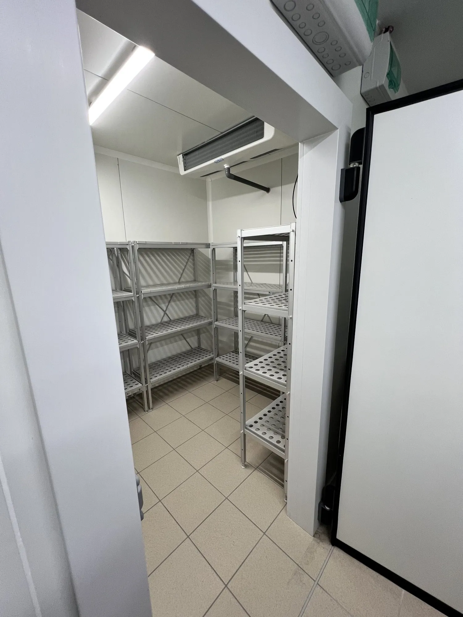 Réserve carrelée avec rayonnages inox vides à côté de la porte isotherme