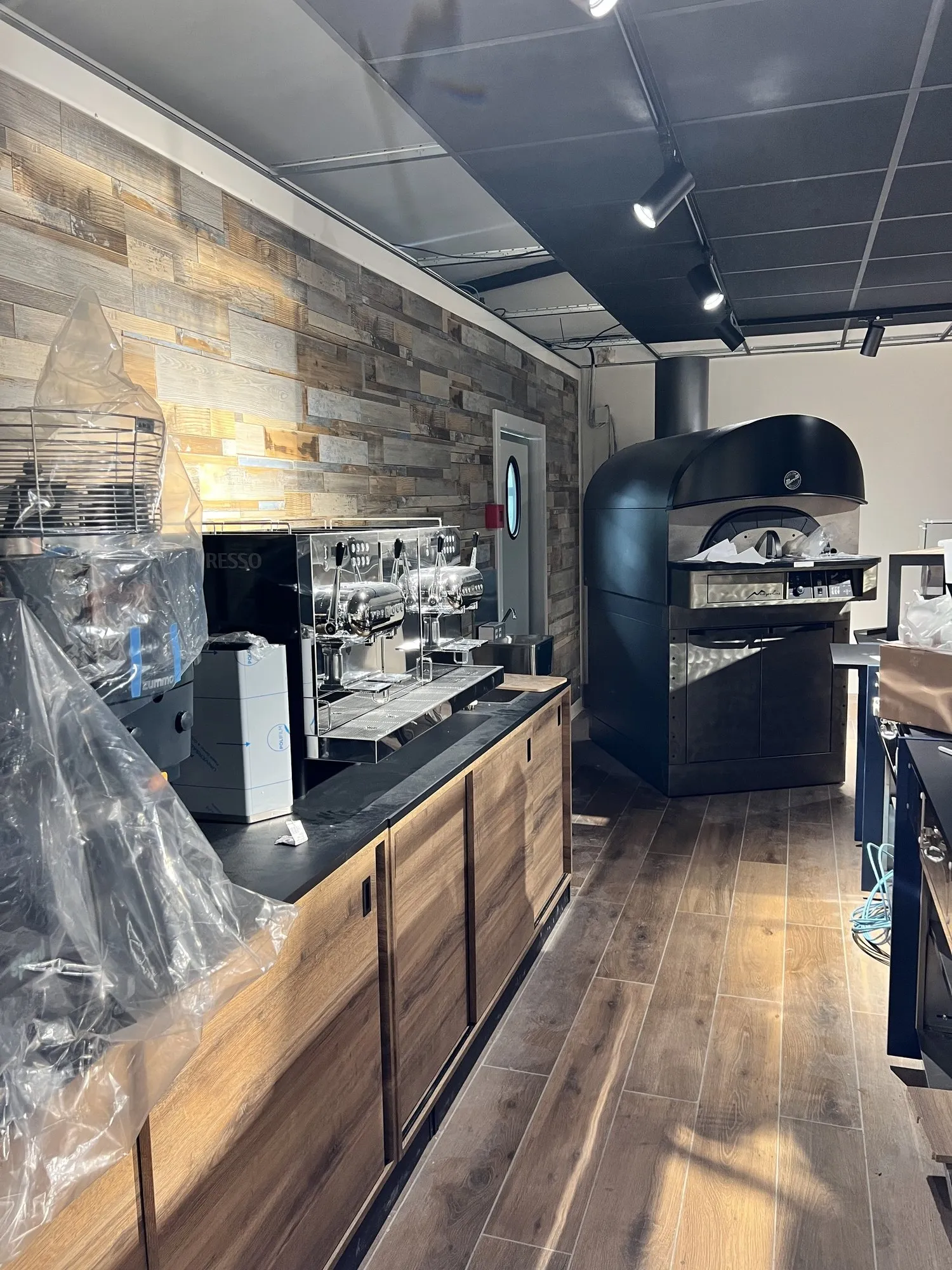 Salle du restaurant en cours d'aménagement : comptoir en bois, machine à café et four à pizza