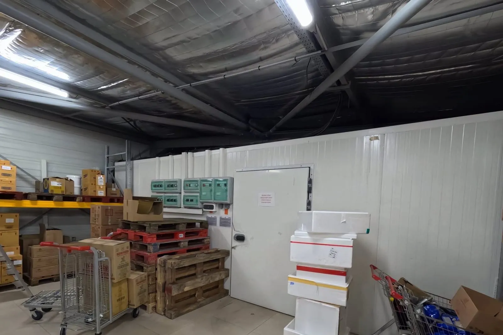 Entrepôt logistique isolé en panneaux sandwich blancs, porte de chambre froide et marchandises sur palettes