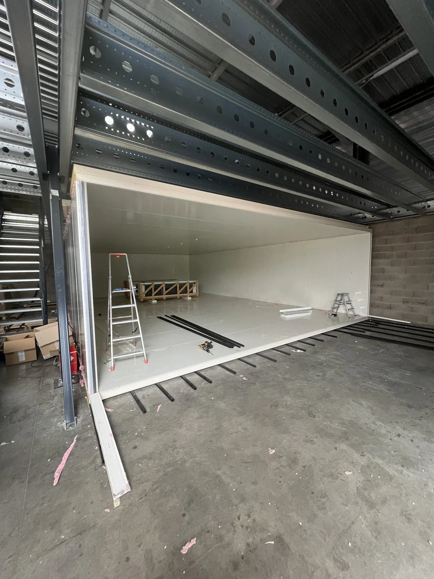 Grande chambre froide en cours de montage dans un bâtiment industriel : panneaux blancs sous une charpente métallique, échelle et béton