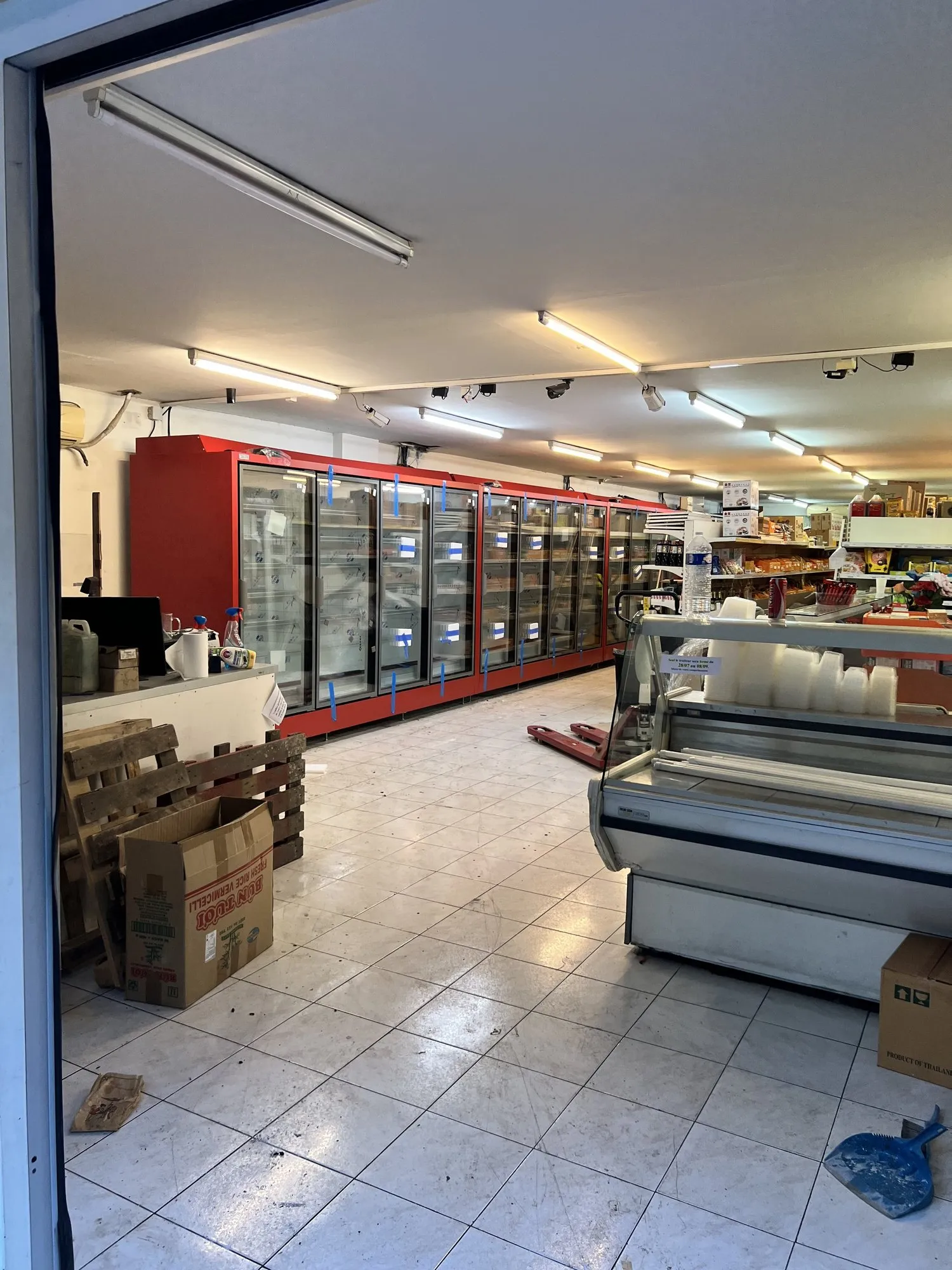 Intérieur de l'épicerie avec ses meubles réfrigérés rouges encore vides et des cartons de livraison