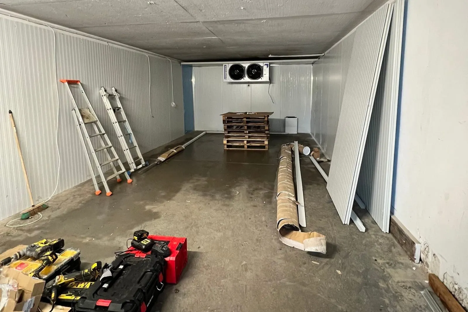 Montage d'une grande chambre froide : panneaux sandwich en cours d'assemblage, échelles et outillage au sol