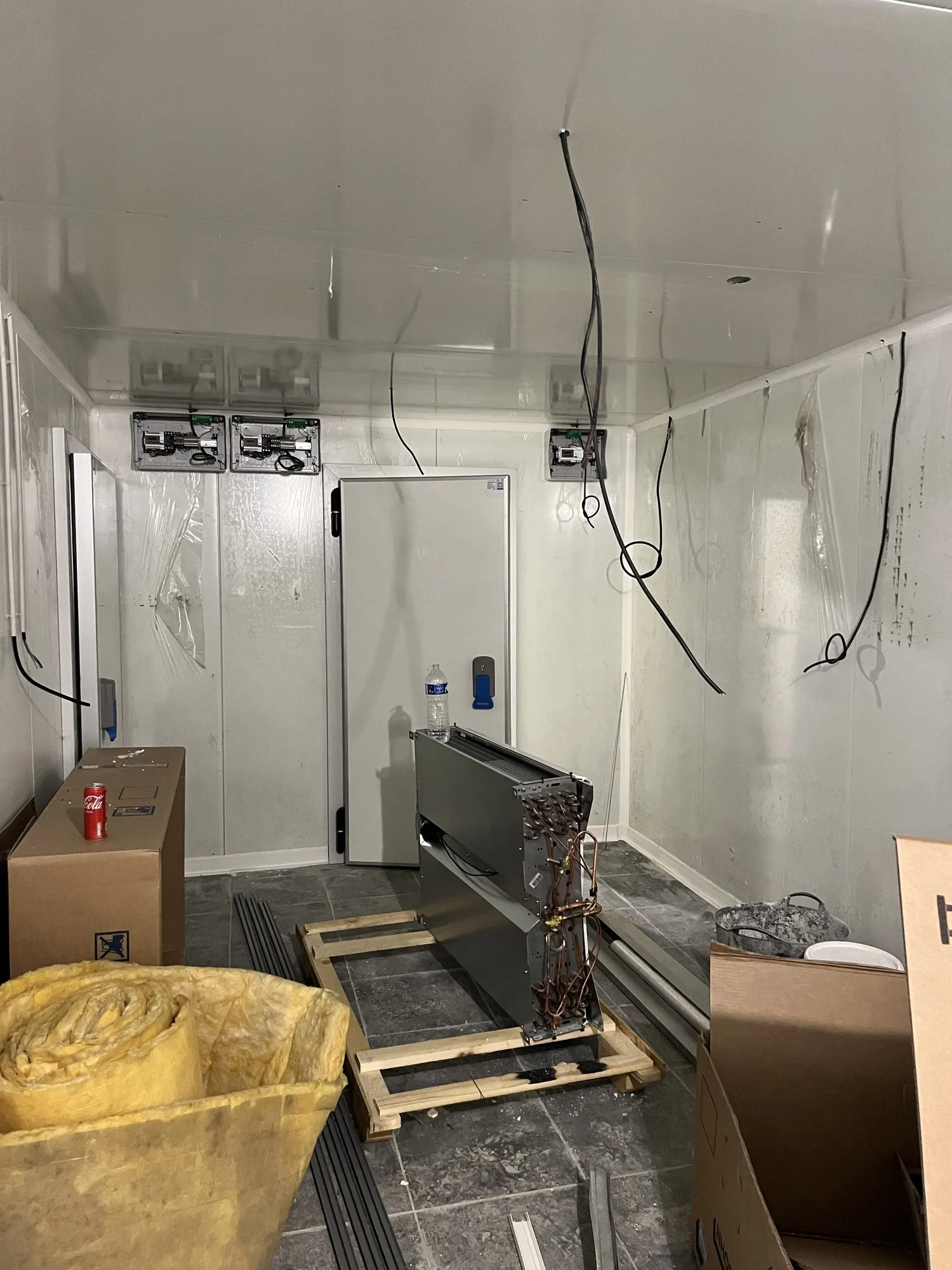 Chambre froide en cours de montage : porte isotherme posée, câbles électriques suspendus, cartons de matériel au sol