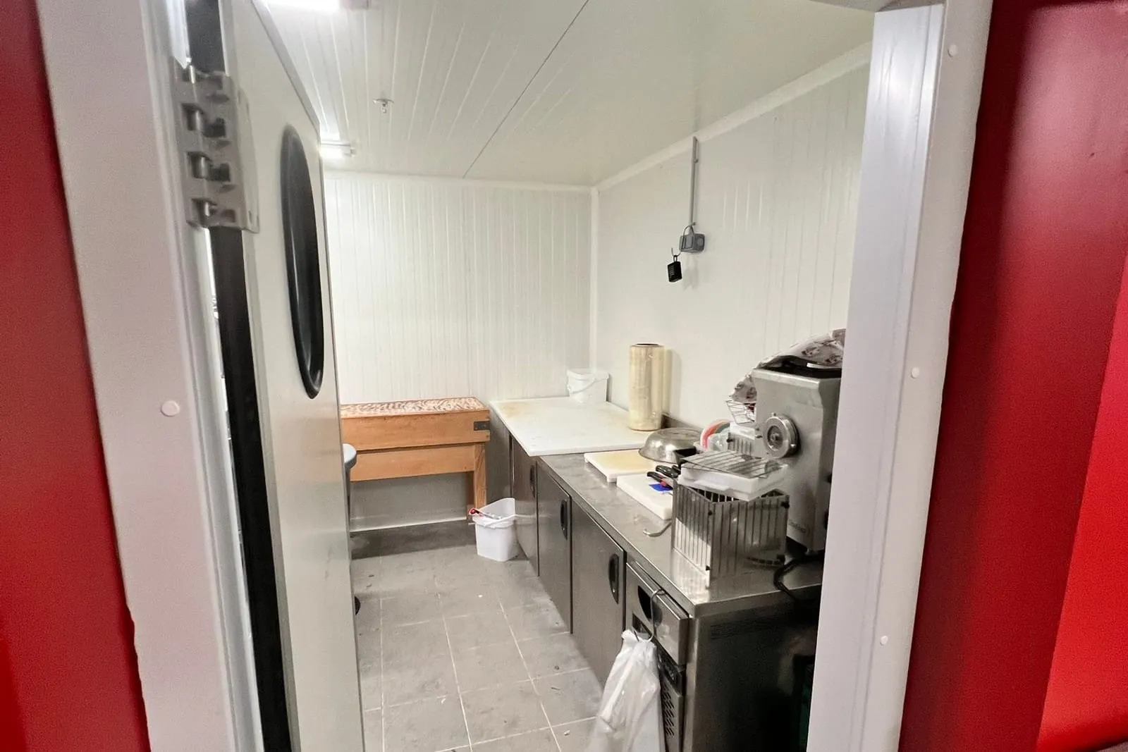 Porte isotherme ouverte sur le local en panneaux blancs, hublot rond et parement rouge autour de la porte