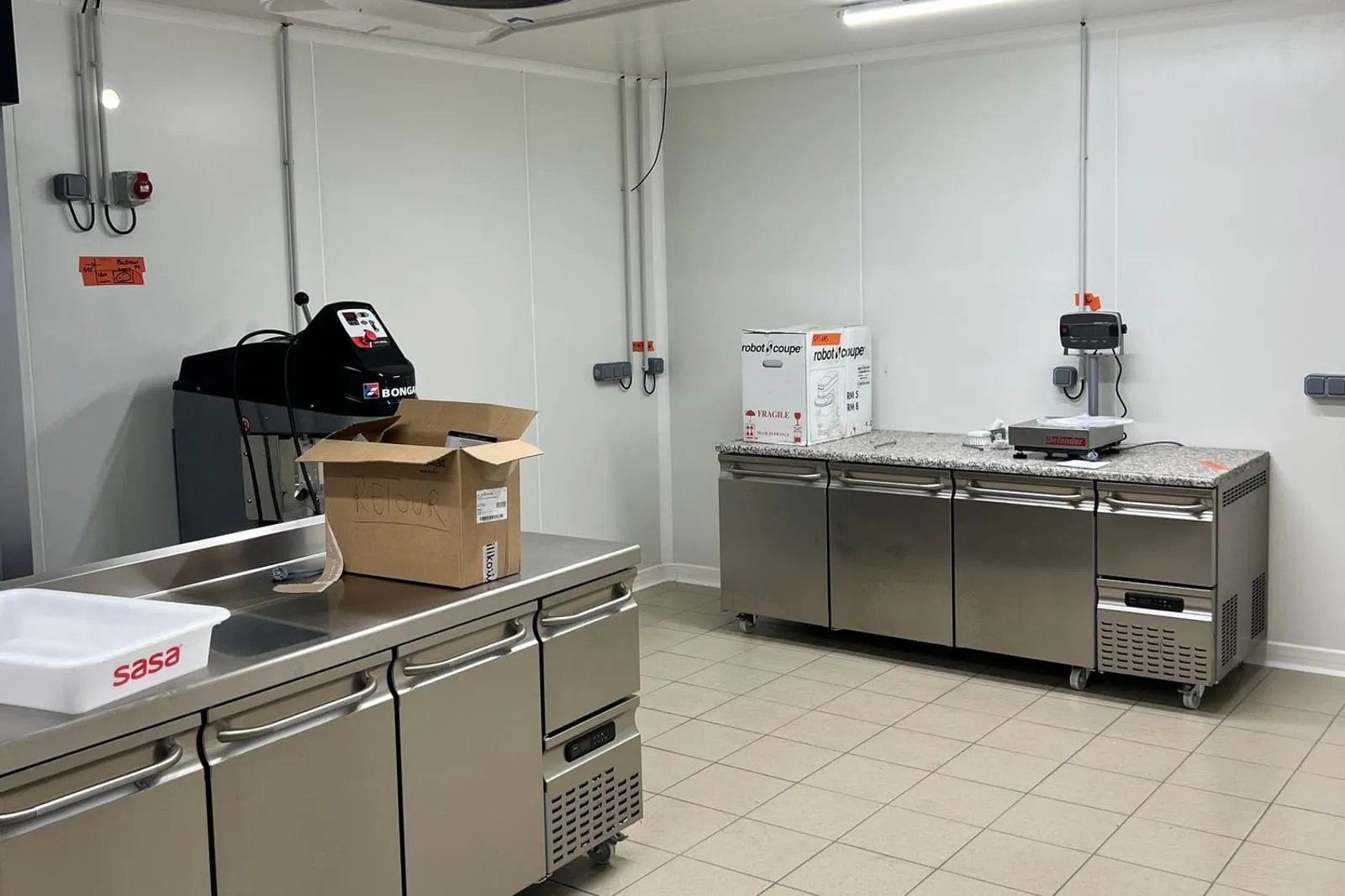 Cuisine professionnelle équipée de meubles réfrigérés en inox et d'un évaporateur plafonnier, sol carrelé