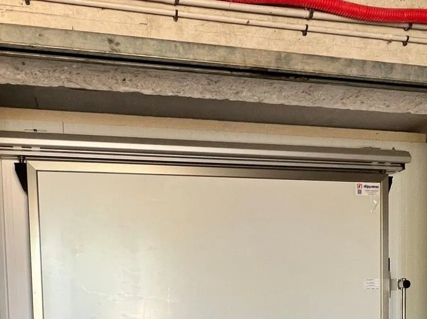 Porte frigorifique isotherme blanche posée dans une réserve, avec sa gaine électrique rouge en applique