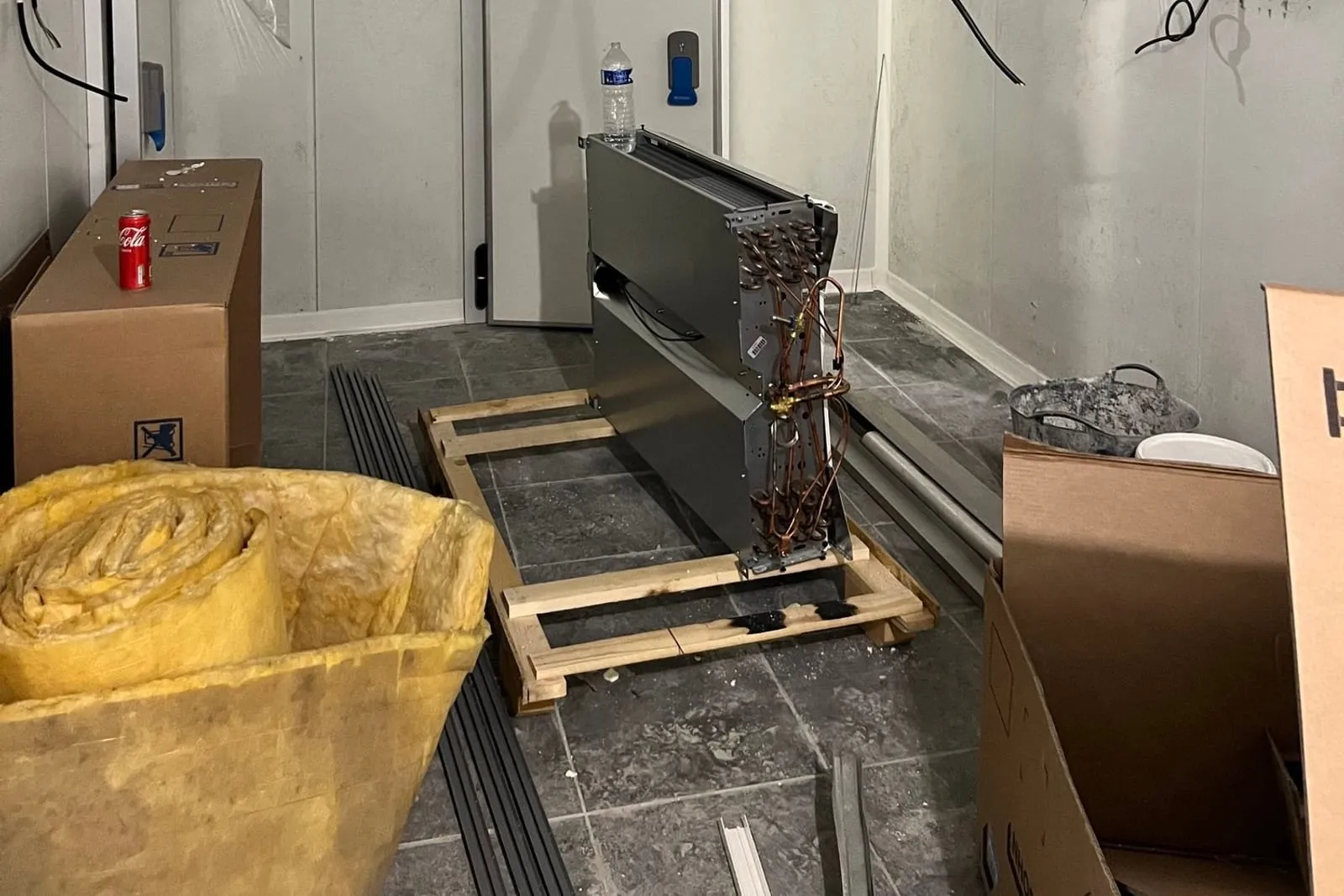 Chantier de pose de panneaux sandwich : panneaux, rouleau d'isolant et cartons de matériel devant la porte de la chambre froide