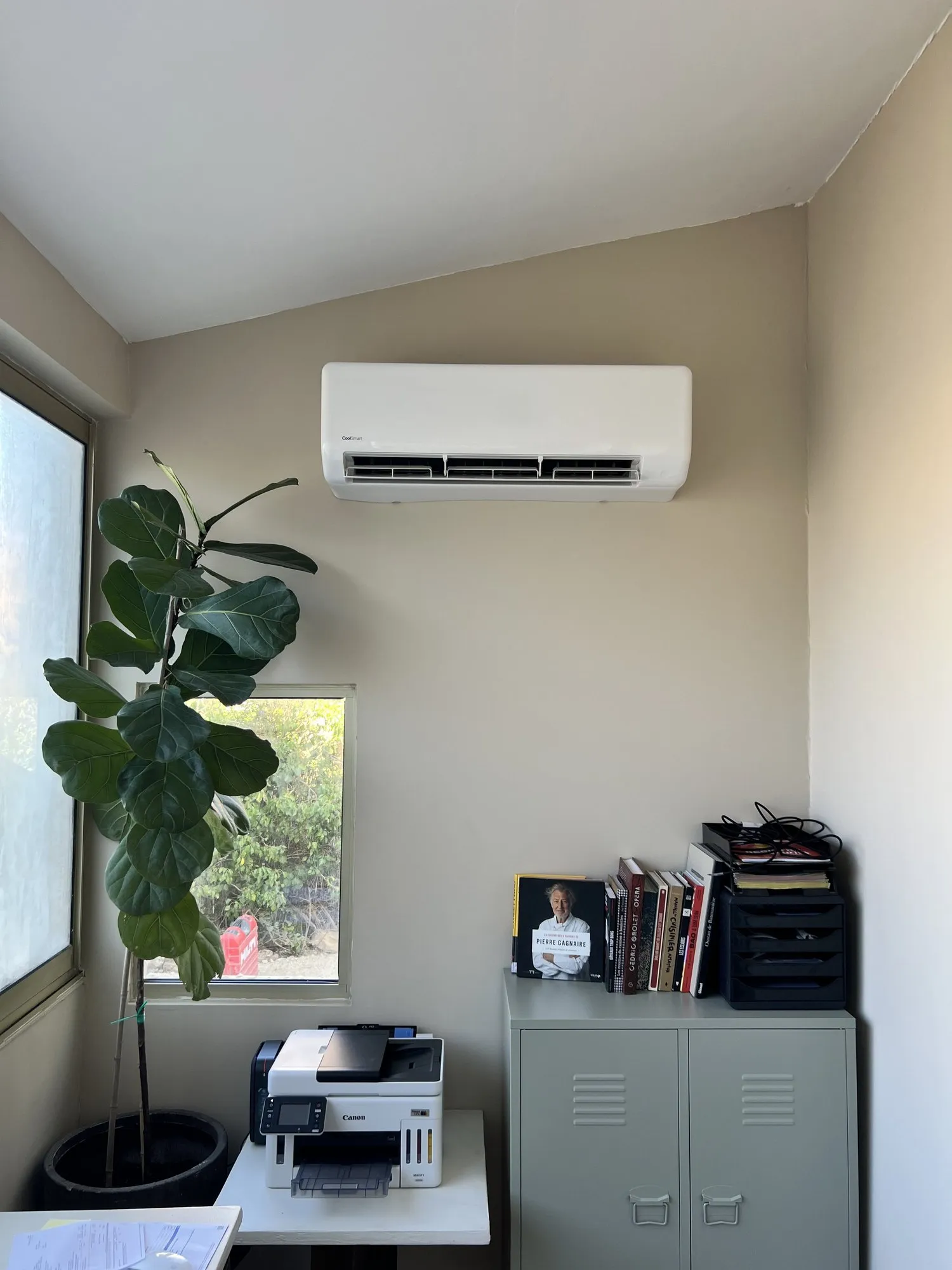 Bureau avec unité de climatisation murale au-dessus d'une armoire, imprimante et plante verte