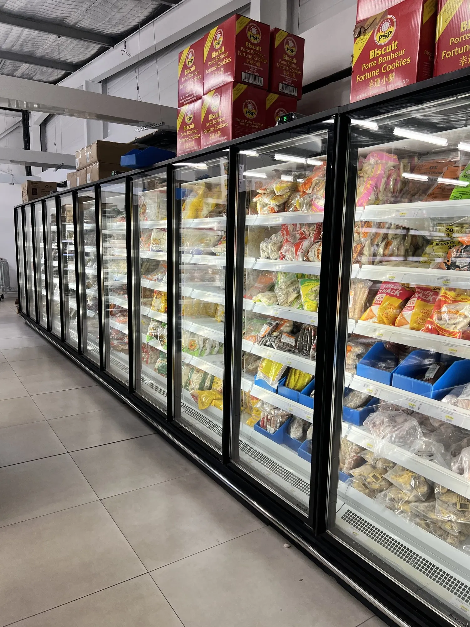 Longue rangée d'armoires réfrigérées à portes vitrées remplies de produits surgelés dans une allée de supermarché
