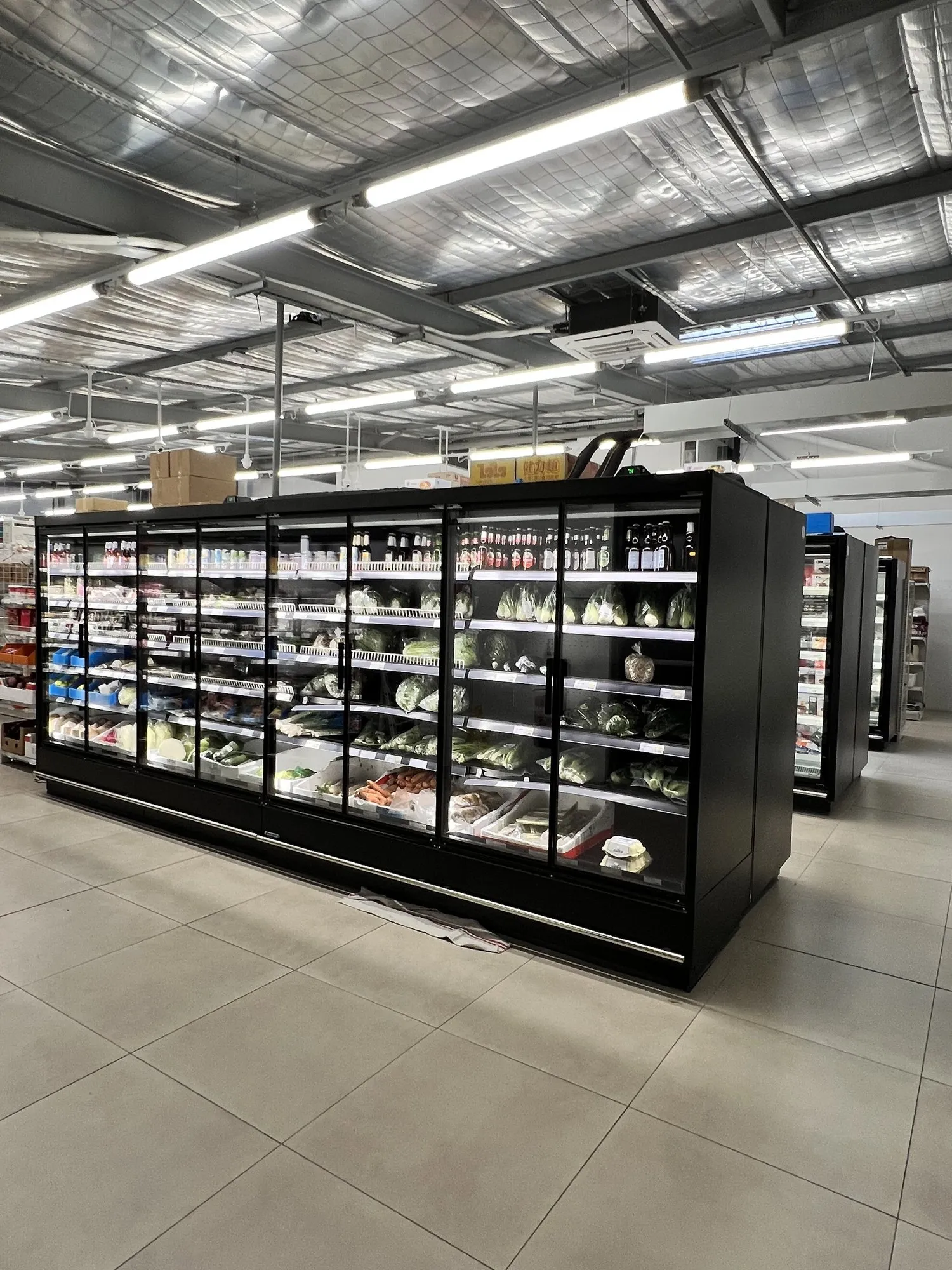 Vitrines réfrigérées noires de légumes et produits frais sous la charpente métallique du magasin